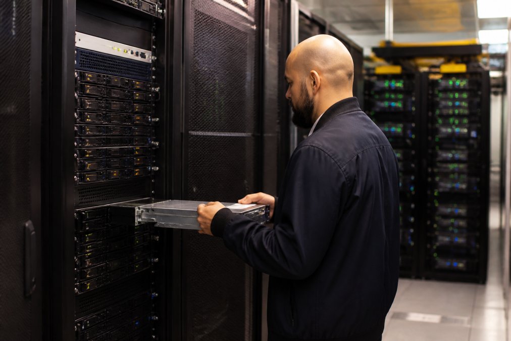 IT professional monitoring backup systems across multiple screens in a modern server room with blue and green indicator lights