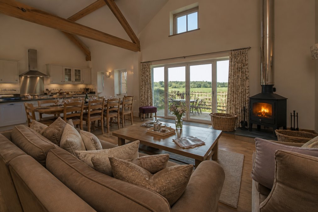 Spacious, bright self-catering barn interior with fully equipped kitchen, log burner, and countryside views through large windows, family gathering space with comfortable seating