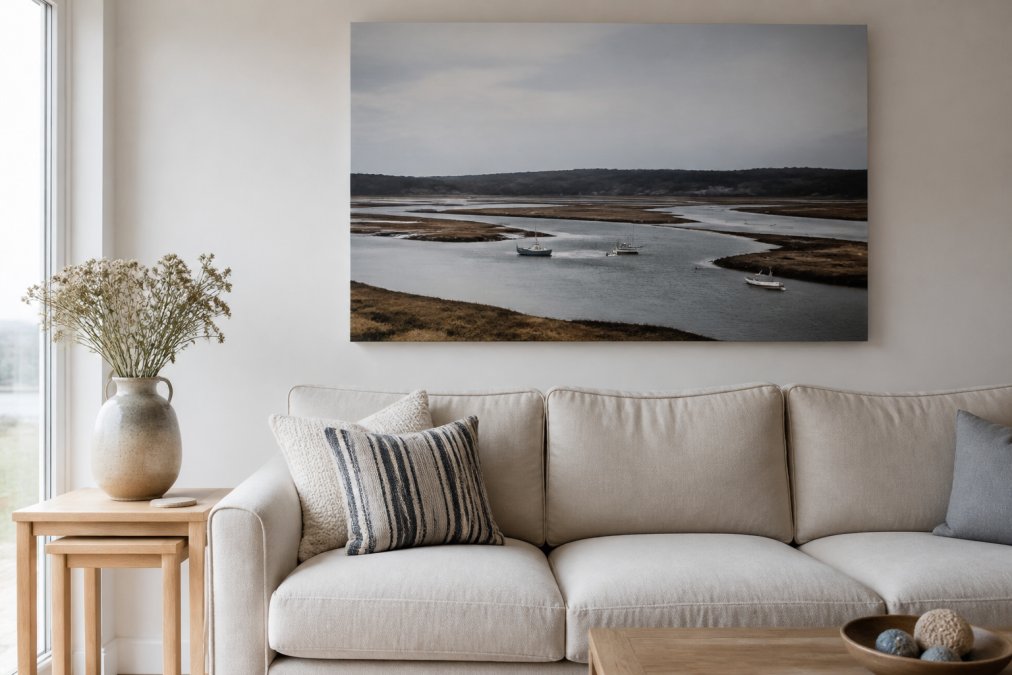 A bright British living room with a neutral linen sofa, a single large coastal canvas print of a tidal estuary hanging above it, and a light wooden side table with a ceramic vase nearby