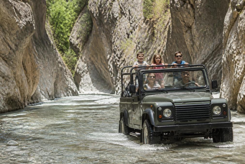 Çocuklar ve ebeveynler 4x4 jeepte oturmuş, Saklıkent Kanyonu'nun doğal güzelliği arka planda görülüyor, kanyon duvarları ve su akışı net görünüyor