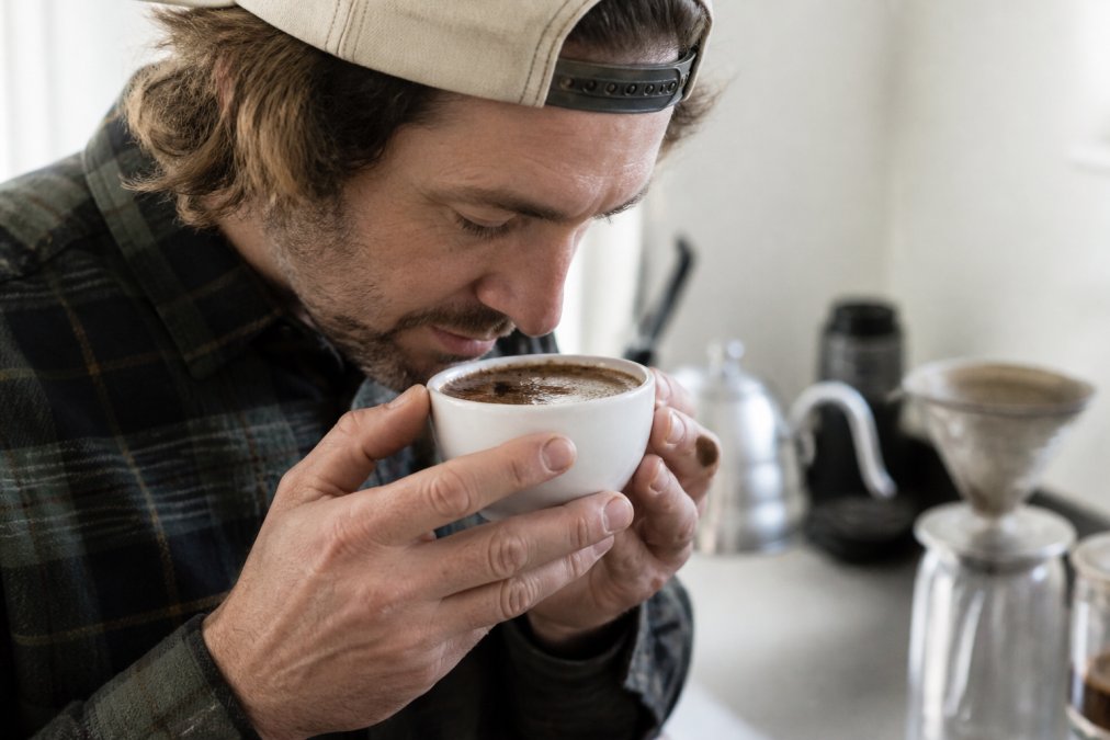 A home barista examines the rich crema in a white cupping bowl to evaluate coffee extraction balance.