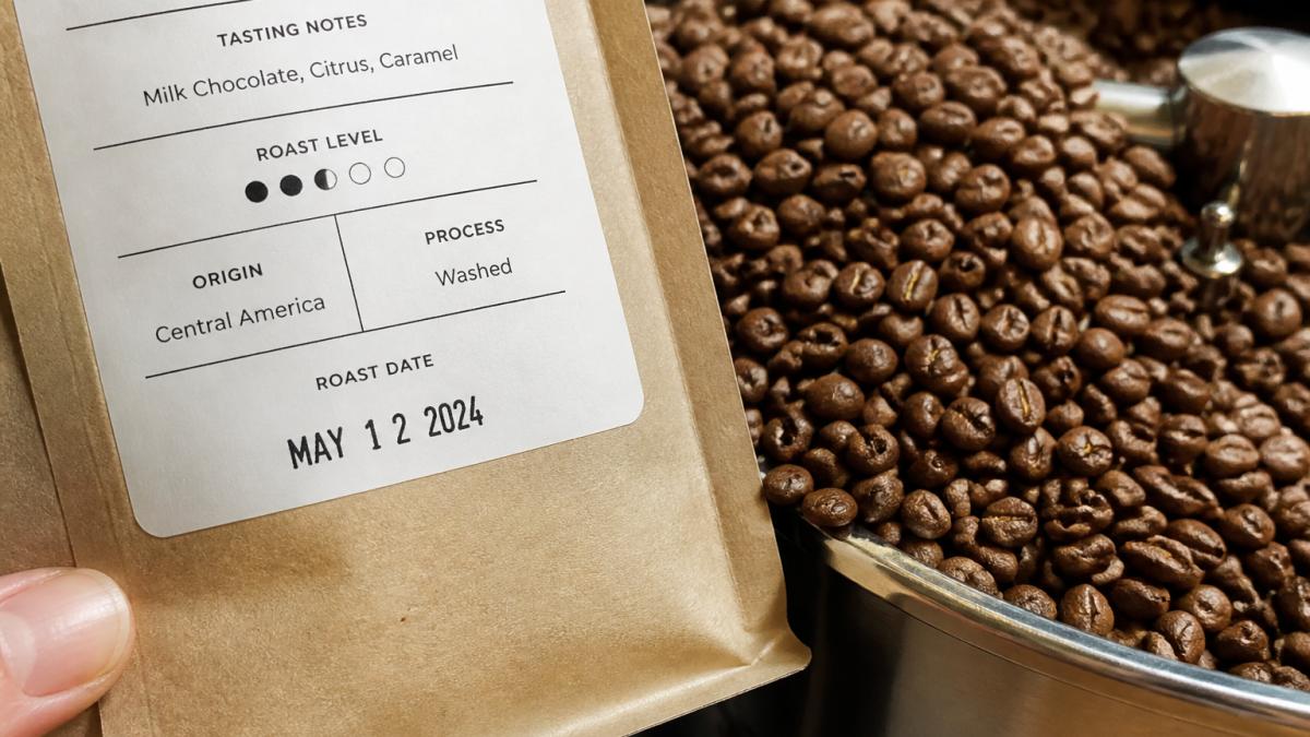 Close-up of a coffee bag label showing a printed roast date with fresh roasted beans visible in the background