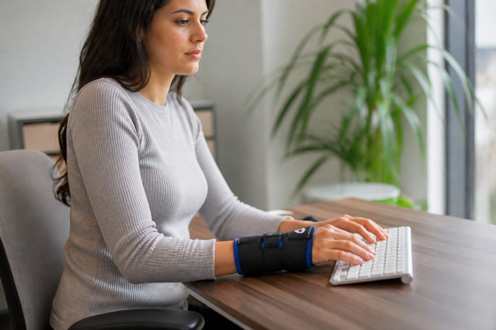 Person wearing wrist cold compression sleeve while working at desk, demonstrating comfort and mobility during typing and daily activities in natural office lighting