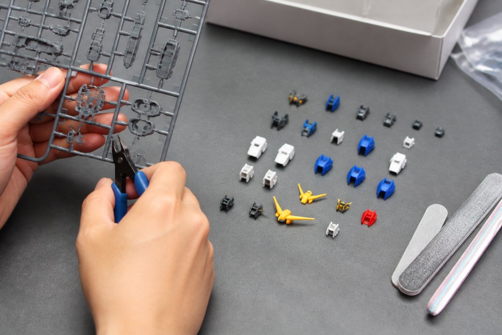 Hands carefully removing plastic parts from a sprue using nippers, with cleaned parts arranged in organized groups and sanding sticks nearby on a clean gray work surface