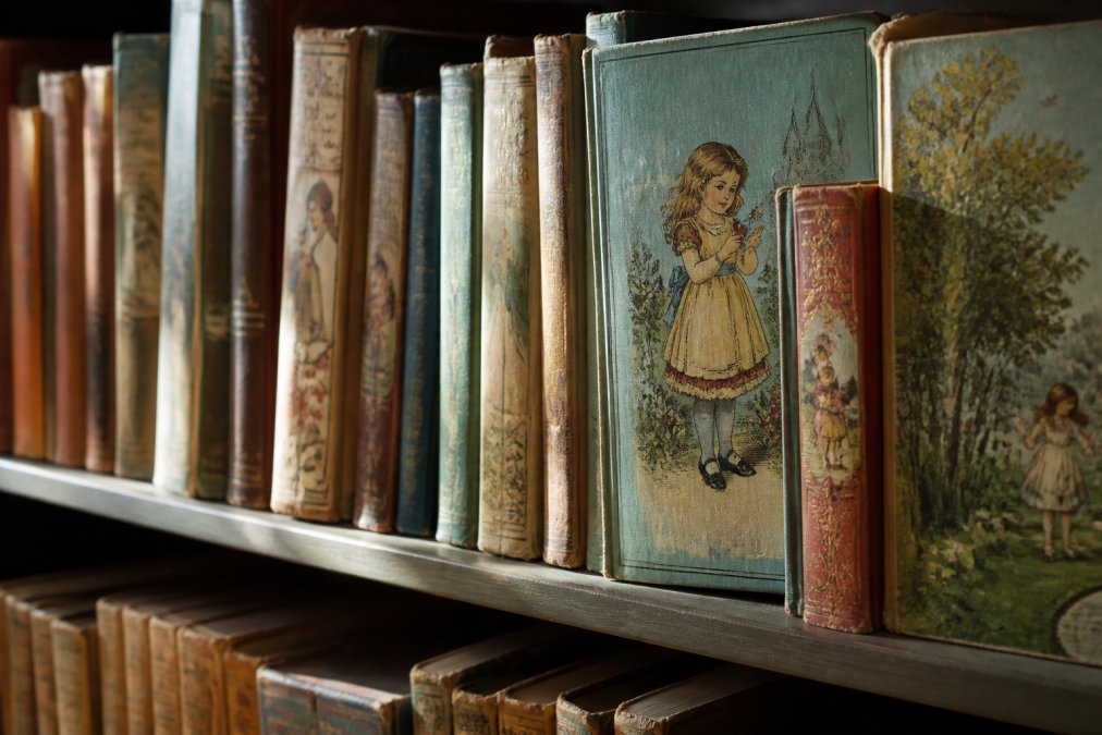 Close-up of vintage children's books displayed on a shelf with ornate spines and colorful covers, natural light highlighting aged paper and detailed illustrations