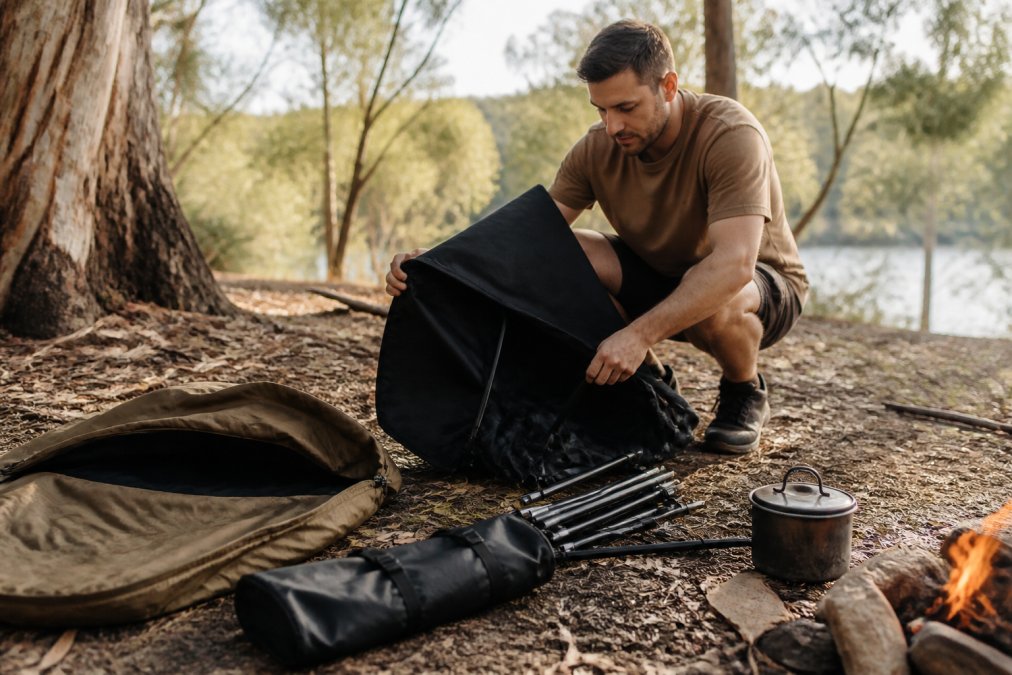 A person sitting comfortably in a compact black camping chair at an Australian campsite, with a swag and a billy nearby, morning light, relaxed posture