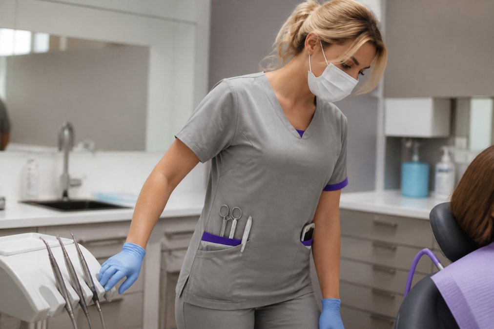 Close-up of dental assistant wearing well-fitted scrubs with visible utility pockets holding scissors, explorer, and phone, demonstrating practical pocket functionality and how proper fit allows comfortable movement and tool access during active chairside work