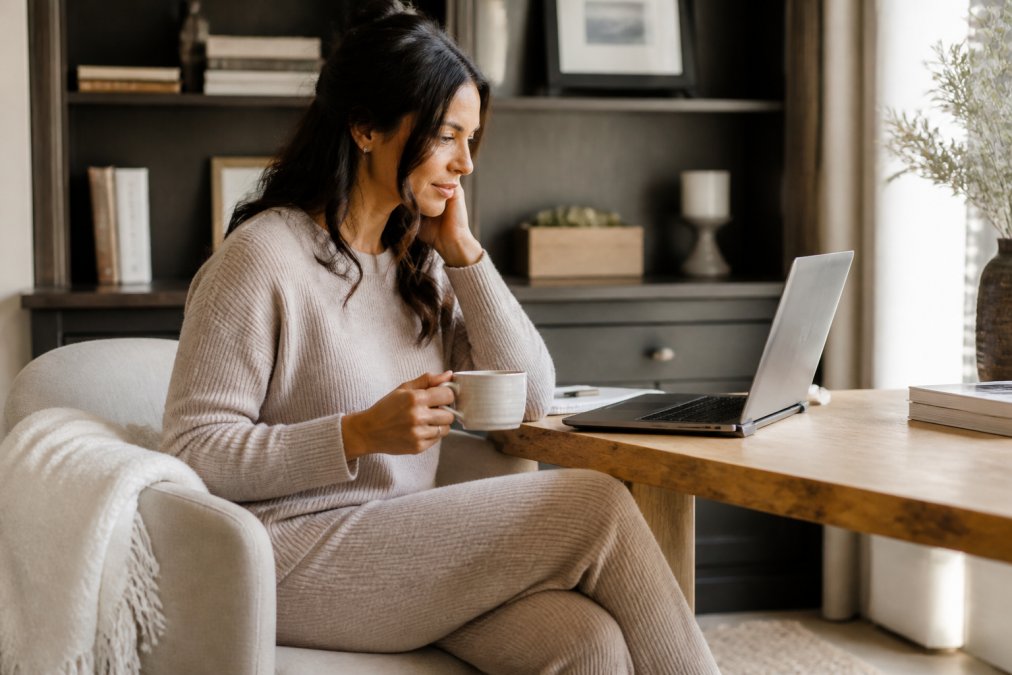 A woman working from a bright home office wearing a matching knit lounge set, sitting at a desk with a laptop and coffee, looking comfortable and put-together