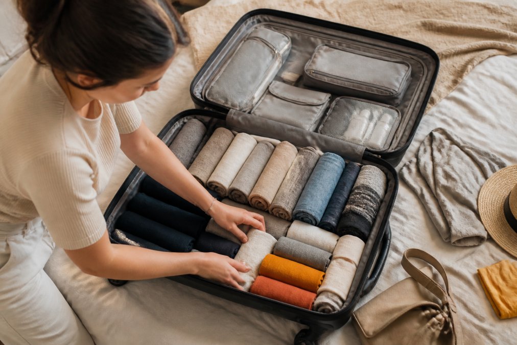 Valise ouverte bien organisée vue de dessus, avec vêtements pliés selon la méthode Marie Kondo, accessoires rangés dans des pochettes de rangement compartimentées, des chaussettes roulées dans les espaces vides, montrant une optimisation d'espace efficace et méthodique
