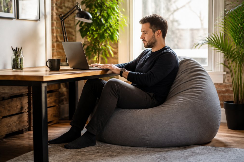 Personne assise confortablement sur un beanbag ergonomique à un bureau de télétravail, avec un ordinateur portable et une bonne posture visible, dans un espace de travail lumineux à domicile