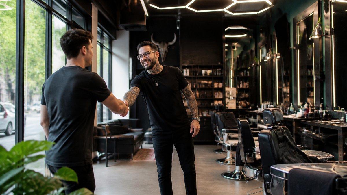 Professional barber welcoming a client in a modern, well-lit salon during a quiet daytime hour, showing the calm and comfortable atmosphere of a visit without waiting