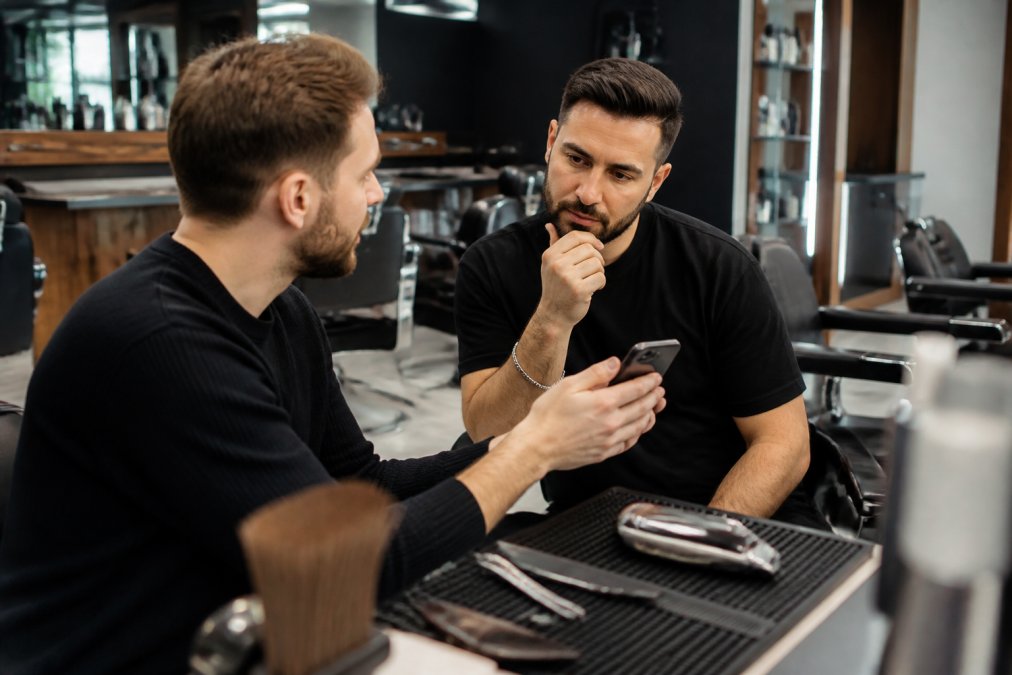Un client montre des photos à son barbier pour éviter les coupes ratées homme dans un salon moderne.