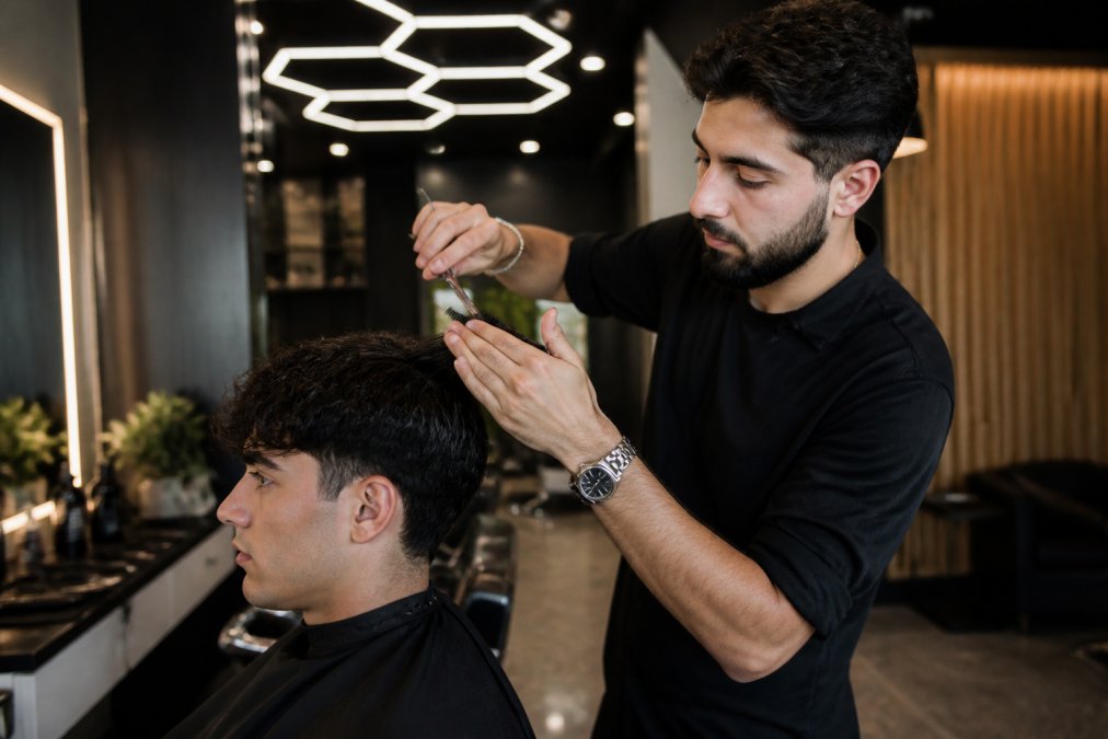 Un barbier professionnel sectionnant les cheveux épais d'un client à l'aide de ciseaux et d'un peigne, dans un salon moderne avec un éclairage hexagonal distinctif au-dessus du fauteuil