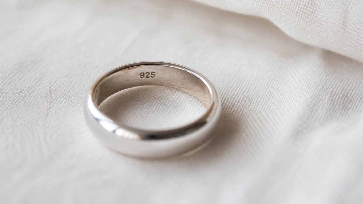 Gros plan sur une bague en argent sterling posée sur un tissu clair, montrant le poinçon 925 gravé à l'intérieur de l'anneau, lumière naturelle douce