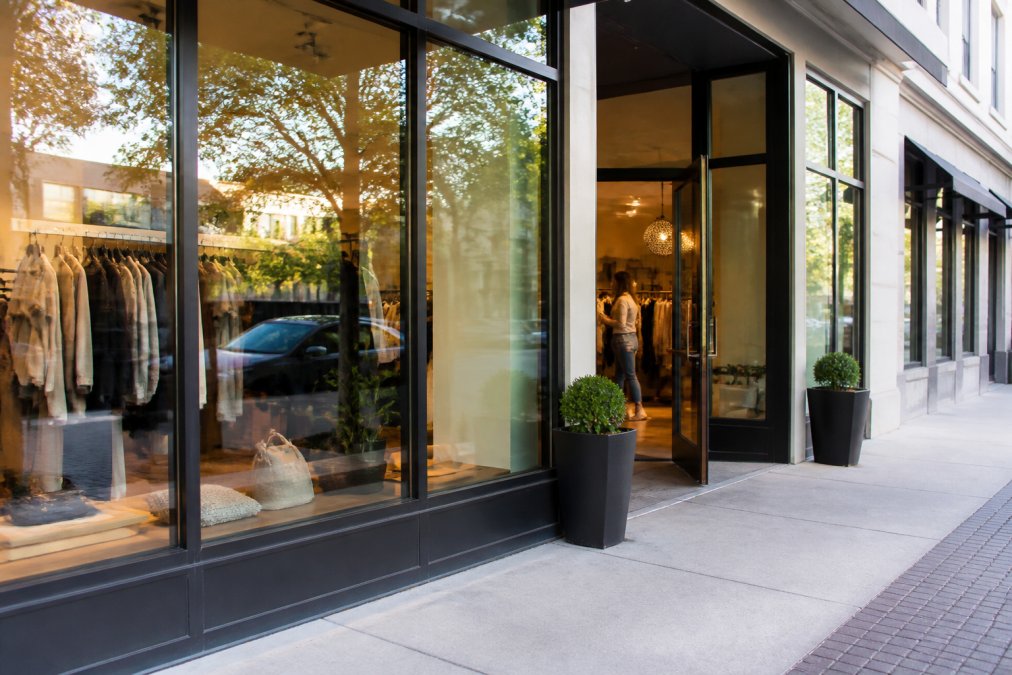 Bright storefront window with spotless glass displaying retail merchandise, professional storefront entrance with gleaming doors and clean sidewalk, customers visible inside shopping