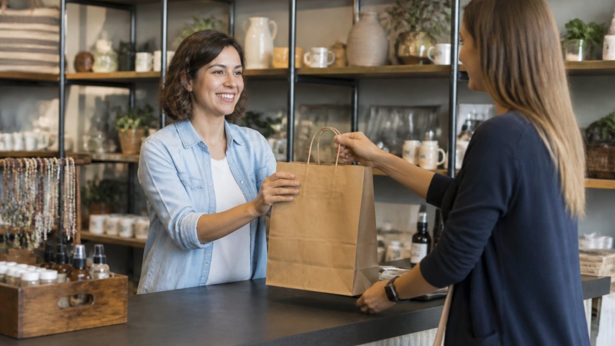 Retail store owner assisting customer at checkout counter in modern, well-lit retail environment with shelving and products visible