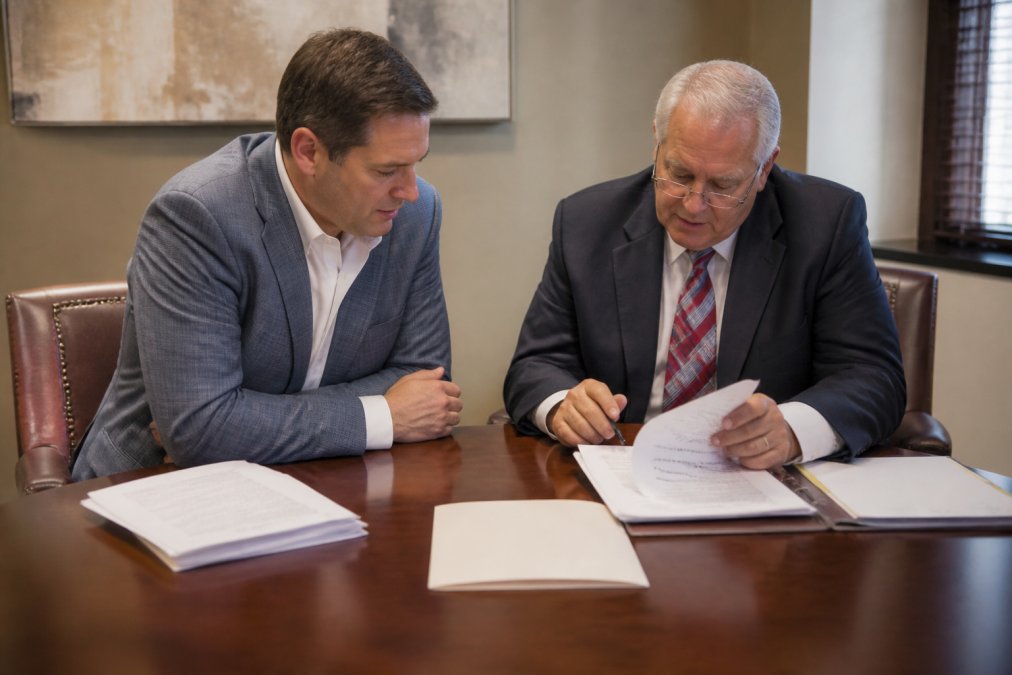 A business owner and a lawyer in a quiet office reviewing a contract and case documents together at a wooden conference table