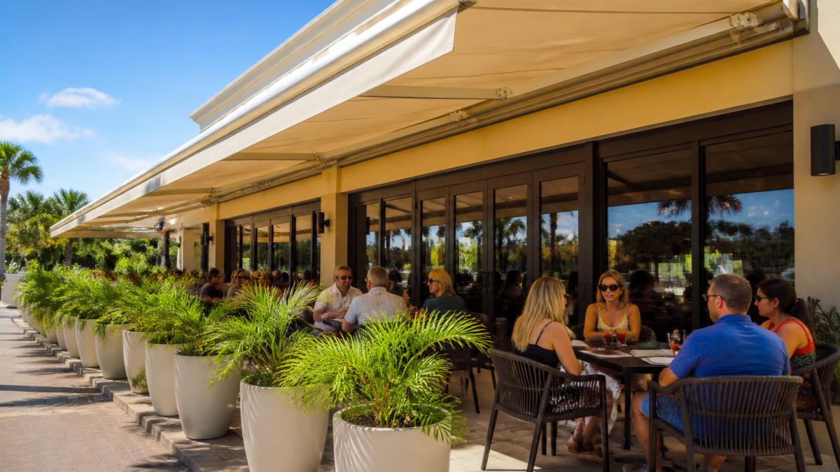 Diners seated under a retractable fabric awning as one of the popular patio shade systems at a sunny restaurant.