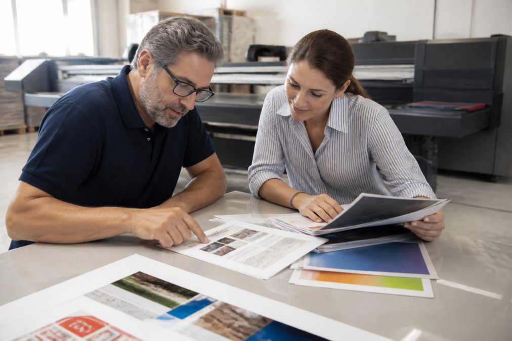 Print manager and client reviewing a commercial printing onboarding checklist and paper samples at a shop table