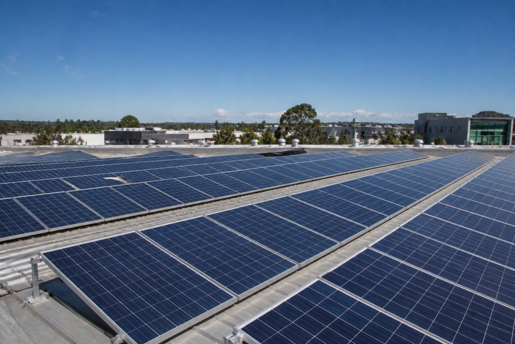 Commercial building rooftop with solar panels installed, showing multiple rows of panels against a clear sky with clear visibility of installation