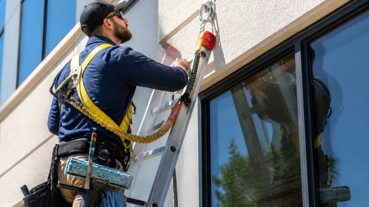 Professional window cleaner checking harness anchor points for window cleaning safety on a commercial building