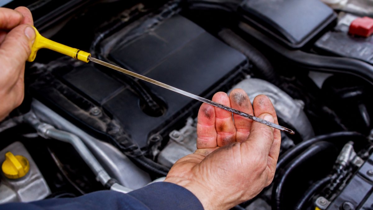 Technician checking dark oil on a dipstick to prevent common car repairs caused by neglected maintenance