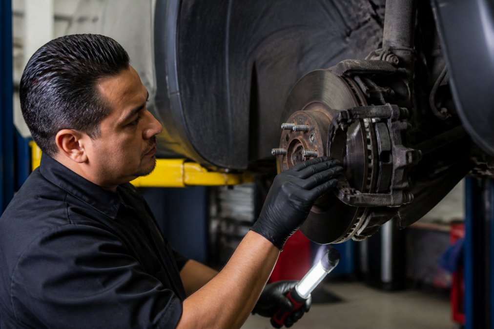 Professional mechanic performing brake pad inspection under vehicle hood, checking wear patterns on rotors and pads with diagnostic tools