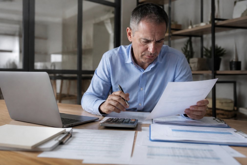 Business owner reviewing financial statements and balance sheet documents at a desk with a calculator and laptop, showing concentration and analysis