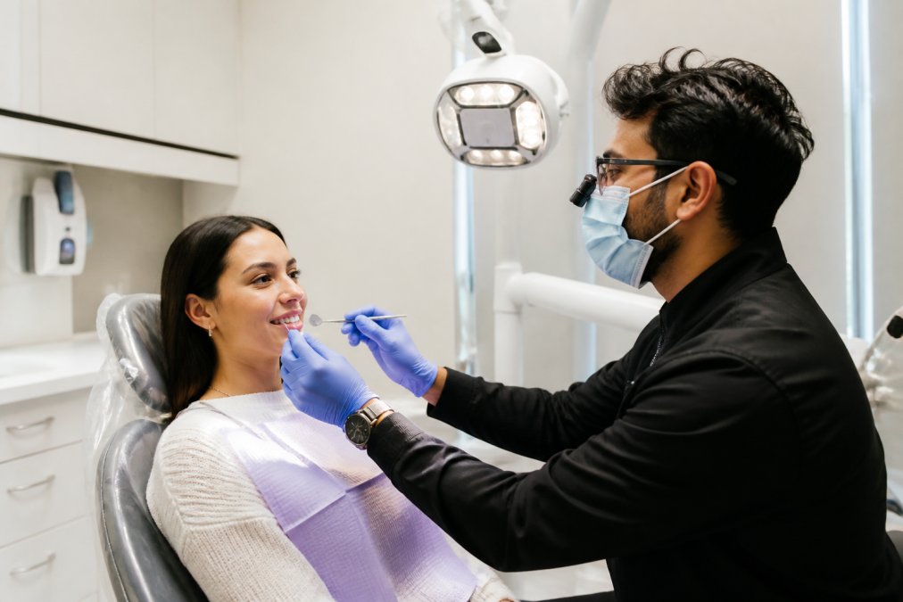 Patient in modern dental chair receiving cosmetic dental consultation with dentist examining smile using digital technology and advanced lighting in bright clinical environment