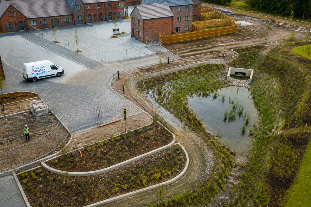 Aerial view of a residential construction site showing permeable paving areas, retention pond, and rain gardens integrated into the landscape during active construction