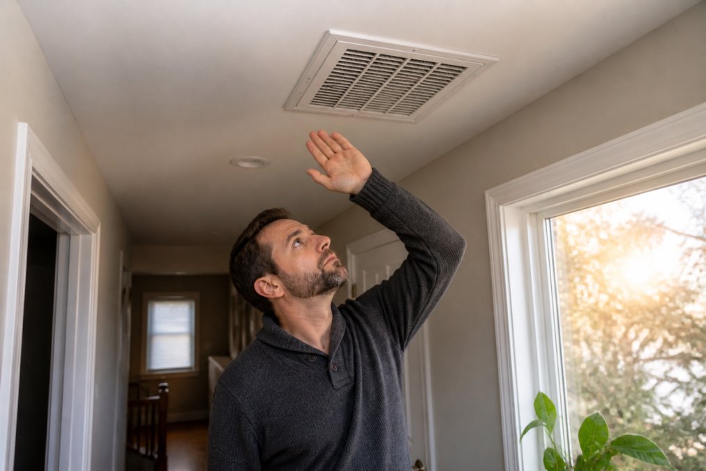 Homeowner checking airflow from a ceiling vent to identify common hvac repair problems