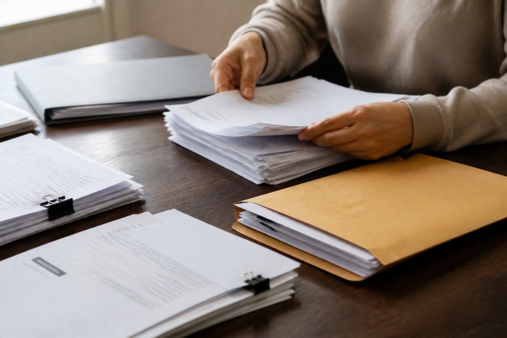 Close-up of hands organizing and reviewing official documents and supporting evidence papers on a work surface, natural lighting