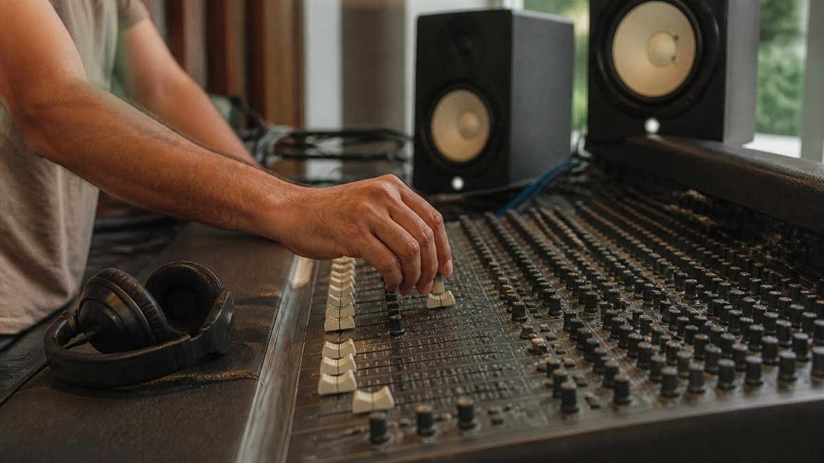 Professional music producer wearing headphones at mixing console with studio monitors visible in modern recording studio with soft lighting