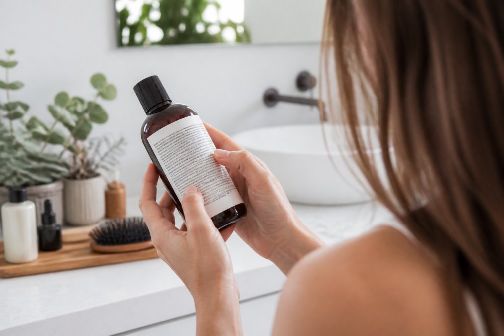 Woman in a bright bathroom reading a shampoo label to check for potential scalp irritants