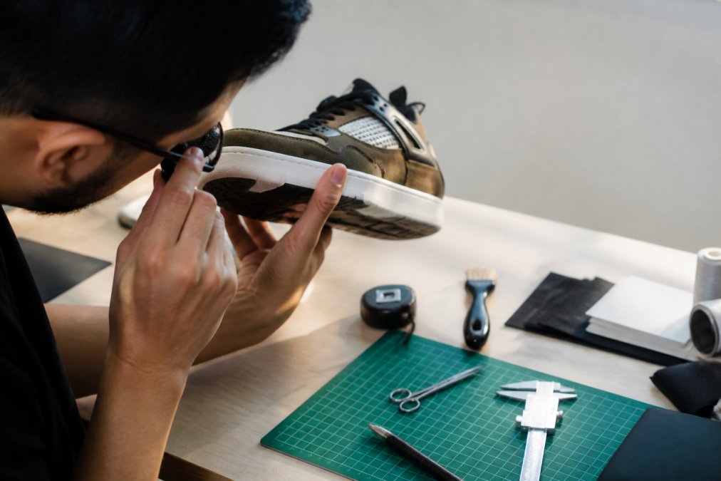 A person closely examining the stitching and sole of a sneaker under bright lighting, holding the shoe up to compare details