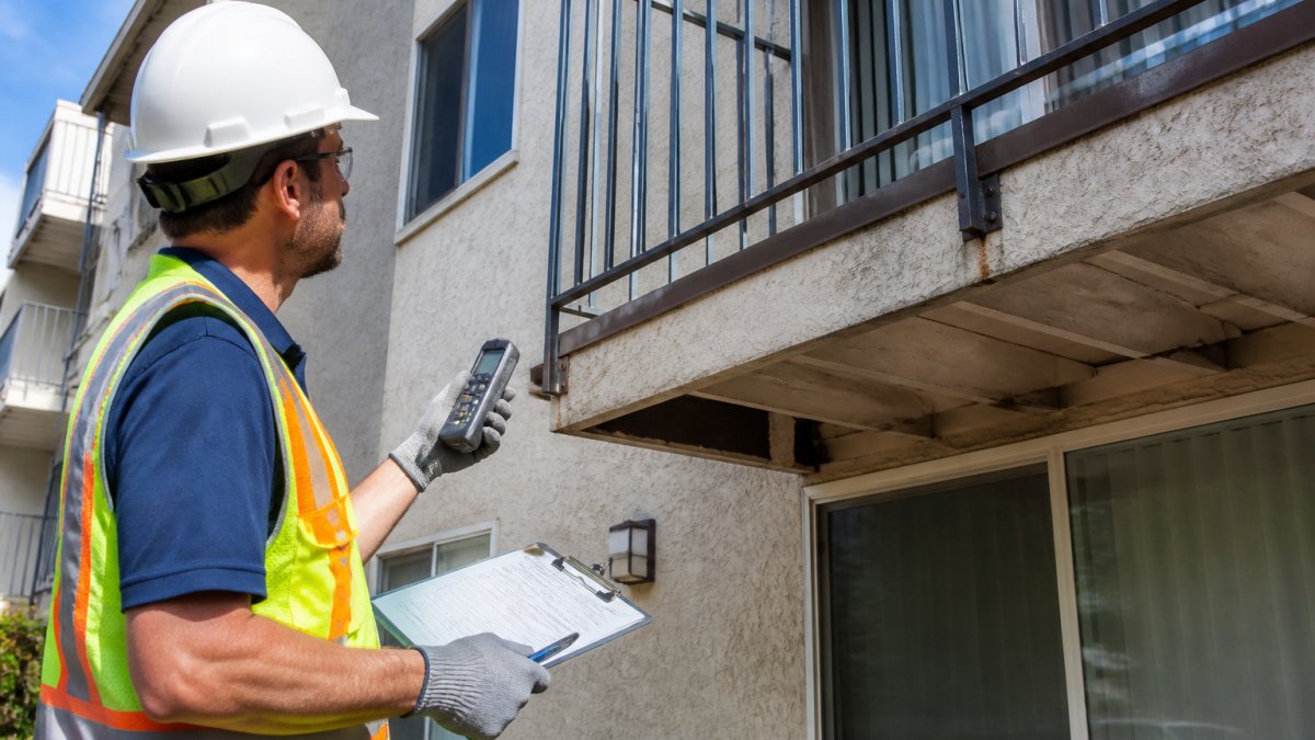 Inspector checking balcony railing and connections for structural defects on a multi-family building