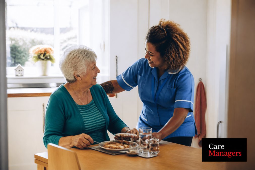 Carer assisting an older adult with daily activities while maintaining eye contact and conversation, showing attentive, respectful interaction in a warm, home environment
