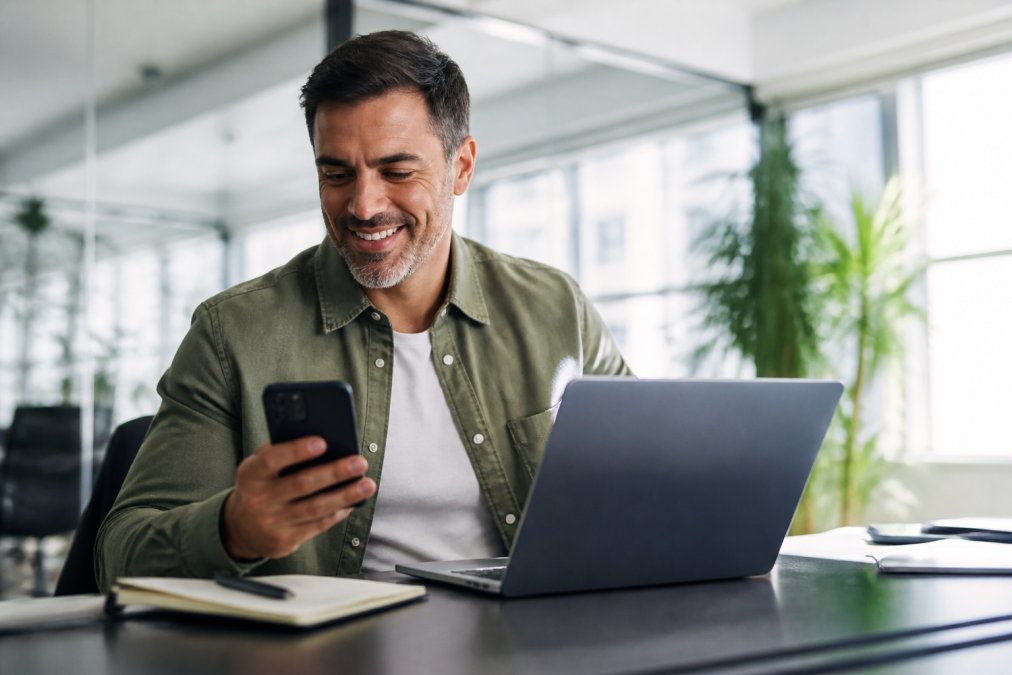 Un profesional sonriente revisando un panel de leads en un portátil, con un teléfono móvil que muestra notificaciones de nuevos contactos, en una oficina moderna y luminosa