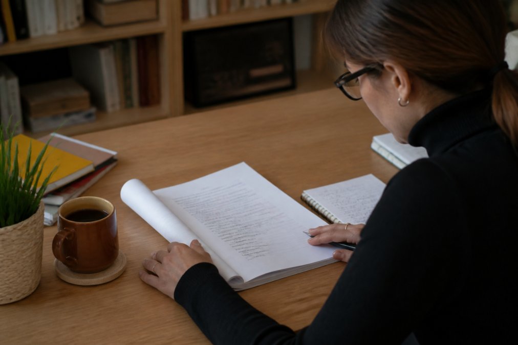 Profesional revisando un documento en su portátil para traducir artículos con café, gafas y notas manuscritas sobre el