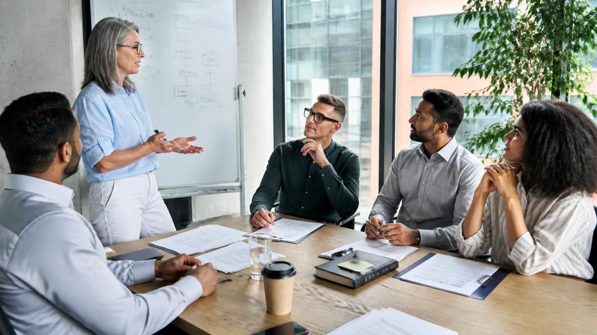 Professional team collaborating in modern meeting room with whiteboard notes on training strategy and skills development, natural light from windows, diverse group engaged in discussion