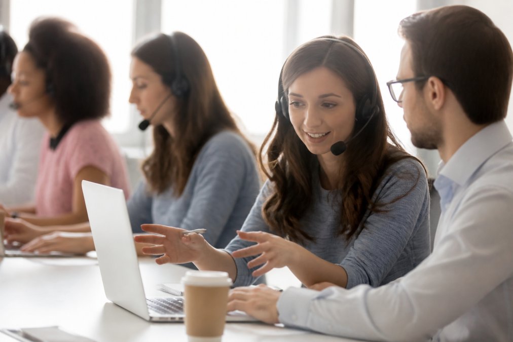 Équipe de support technique en vidéoconférence aidant un utilisateur, plusieurs écrans avec interfaces de plateforme de coaching visibles, environnement professionnel bien éclairé