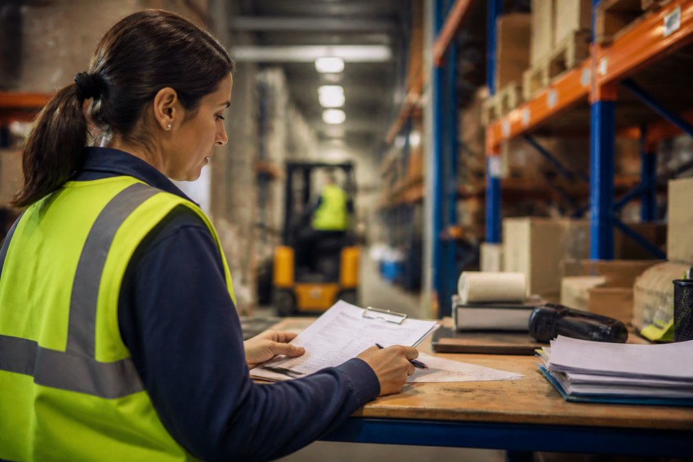 Operations manager reviewing real-time AI-generated insights on laptop at warehouse workstation, with inventory and labor scheduling dashboards visible on screen, natural warehouse lighting