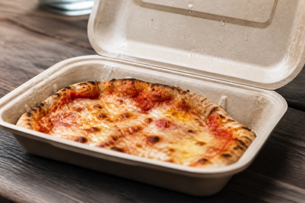 Close-up of a compostable takeaway container holding hot, greasy pizza with visible moisture barrier protecting the food and container structure