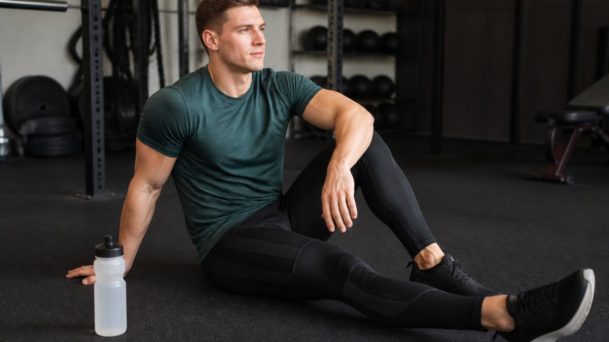 Athlete wearing compression leggings during post-workout cool-down, sitting on gym floor with water bottle nearby, showing proper fit and positioning