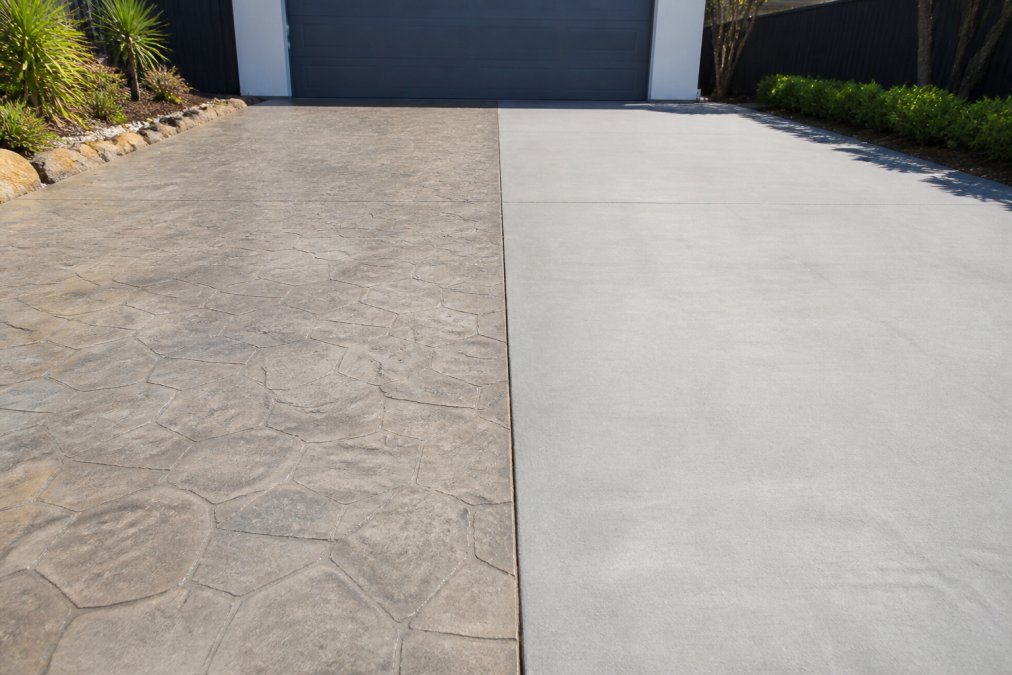 Freshly resurfaced driveway with stamped concrete finish on one side, newly laid solid concrete slab on the other side, demonstrating visual texture and colour differences under bright daylight