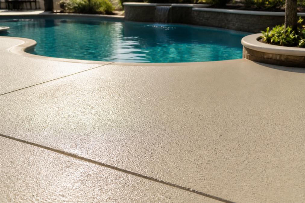Freshly resurfaced pool deck with smooth, slip-resistant coating applied, showing finished aesthetic with clear water, bright sunlight reflecting off the treated surface, and textured finish detail