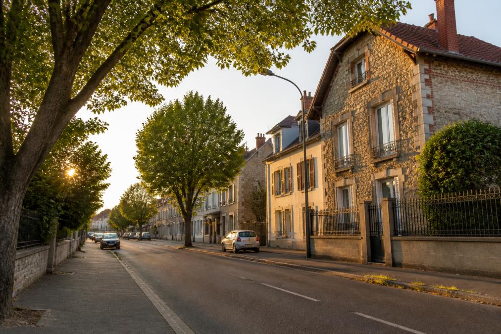 Rue calme et arborée d'un quartier résidentiel de Montluçon, maisons en pierre et petits immeubles en fin d'après-midi, lumière dorée