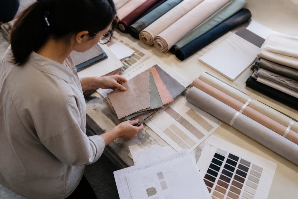 Apparel manufacturer examining fabric samples and swatches on a work table, with color-matched rolls, lab dips, and technical documentation visible, natural overhead lighting