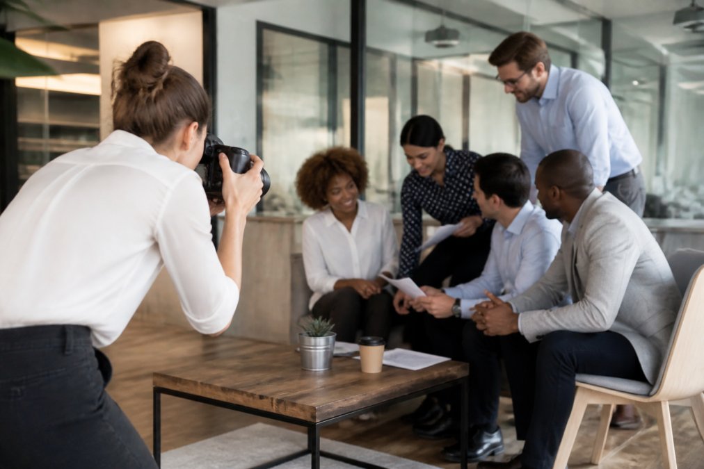 Professional photographer capturing candid moments of business professionals collaborating at a modern conference table, with natural office lighting and environmental context visible