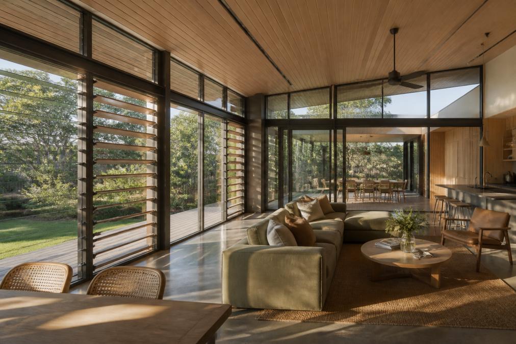 Modern residential home with large north-facing windows, external timber shading devices, and open-plan living spaces designed for natural cross-ventilation, photographed in warm afternoon light